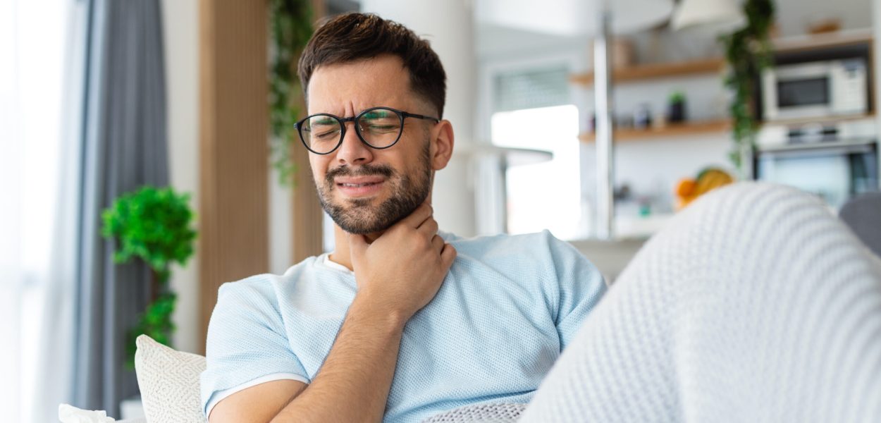 Sick man lying on the couch with high temperature and holding his throat with hand.